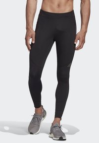 Black athletic leggings with a fitted design, flat seams, and subtle accents. Paired with gray running shoes featuring lacing and mesh.