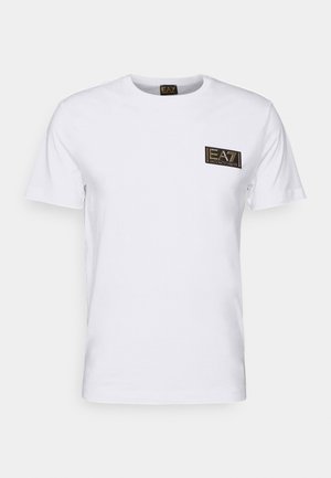 White cotton t-shirt featuring a round neck and short sleeves, with a black and gold logo patch on the left chest. Smooth texture.