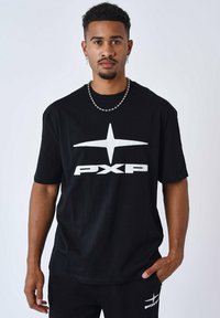 Camiseta de algodón negra con mangas cortas, que presenta un gran logo en blanco de "PXP" y un diseño de estrellas en la parte frontal. Modelo combinado con pantalones a juego.