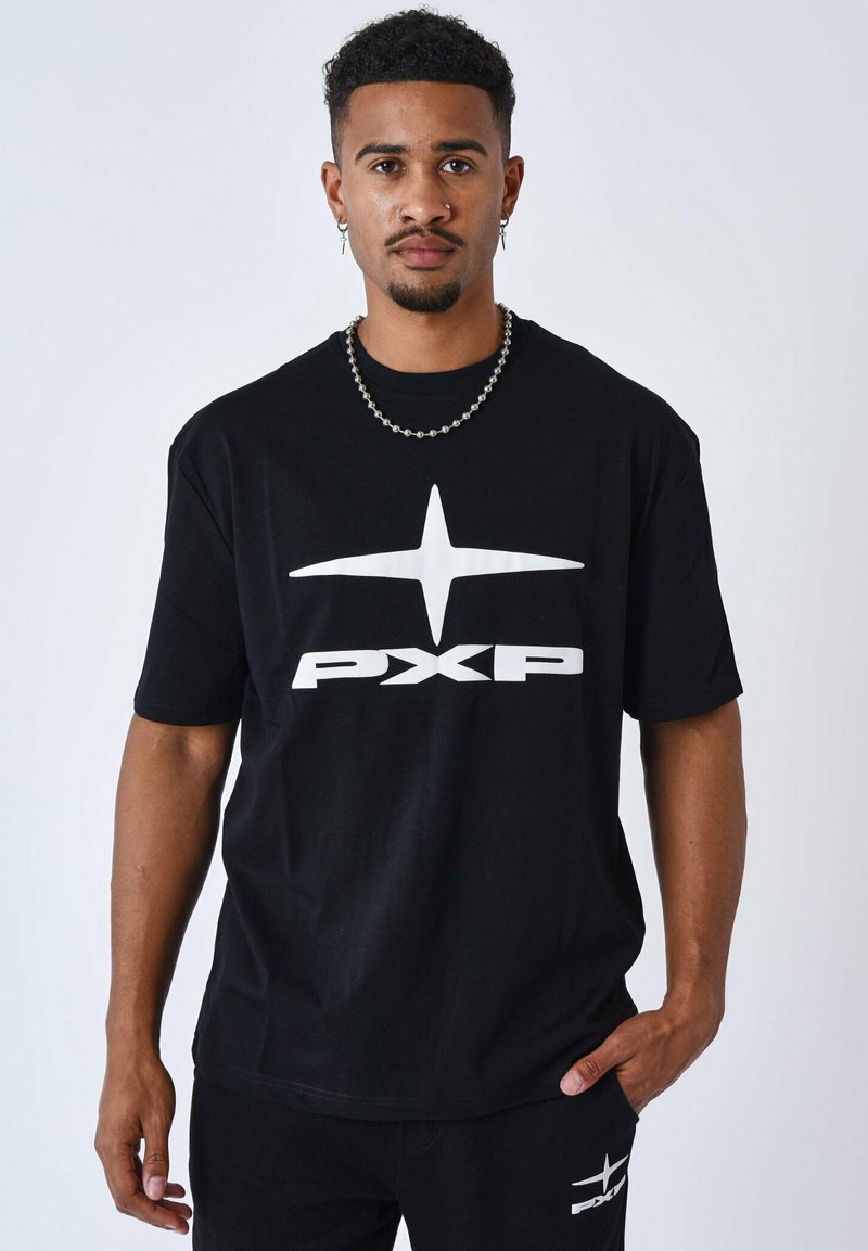 Camiseta de algodón negra con mangas cortas, que presenta un gran logo en blanco de "PXP" y un diseño de estrellas en la parte frontal. Modelo combinado con pantalones a juego.