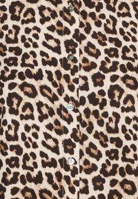 Leopardmønstret stof med store brune og sorte pletter på en beige baggrund, samt sølvknapper langs fronten.