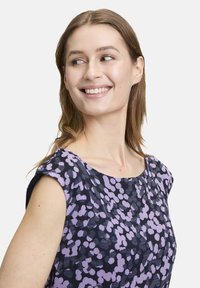Ärmelloses Kleid mit navyfarbener Basis, das ein lila abstraktes Punkte-Muster aufweist, rundem Ausschnitt und strukturierter Stoffqualität.