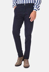 Chinos blu navy con una vestibilità slim, realizzati in tessuto leggero. Presentano passanti per la cintura e tasche frontali, abbinati a scarpe stringate marroni.