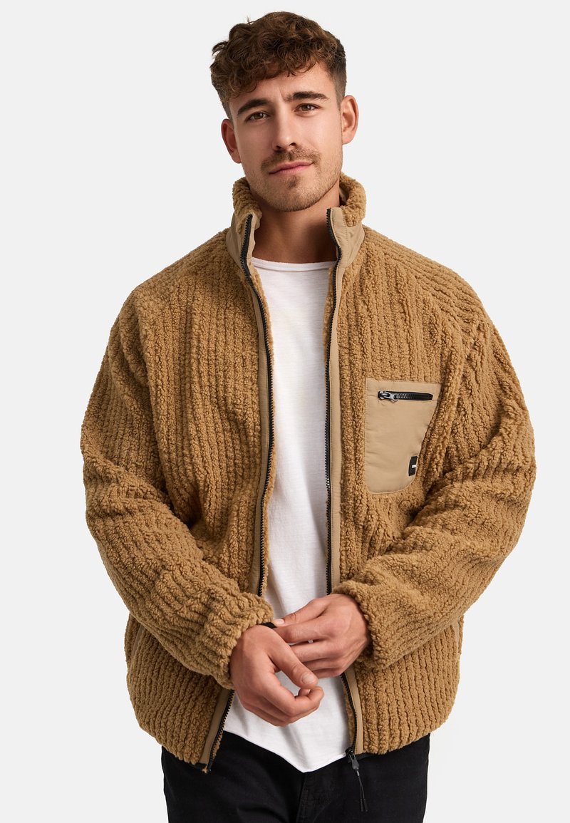 Chaqueta de forro polar texturizado marrón con cremallera frontal y cuello alto. Presenta un bolsillo con cremallera de color beis contrastante en el lado izquierdo del pecho.