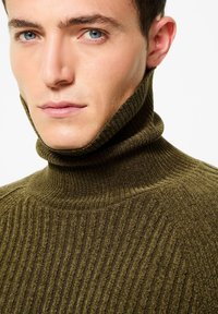 Maglione a collo alto a coste verde oliva con una texture morbida, caratterizzato da un colletto alto e un design aderente.