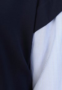 Marineblaues Baumwollmischgewebe, kombiniert mit einem hellblauen Streifenstoff, der ein überlappendes Design und eine glatte Textur aufweist.