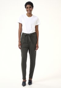 Pantaloni verdi a vita alta con cintura legata, caratterizzati da una texture liscia e un design con gambe affusolate. Abbinati a una t-shirt bianca semplice e scarpe nere.