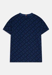 Námořnická modrá tričko s krátkým rukávem s celoplošným tmavomodrým propleteným geometrickým vzorem a malým červeným, bílým a námořnickým pruhem na výstřihu.
