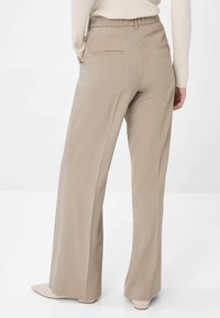 Pantalons large en beige fabriqués à partir d'un tissu texturé avec une taille haute, comportant deux poches arrière. Assortis à des chaussures pointues beiges.