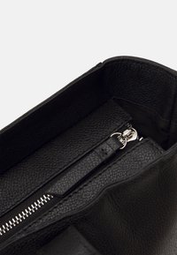 Interno di una borsa a mano in pelle nera con finitura testurizzata, una tasca con zip e hardware della zip in tonalità argentata.