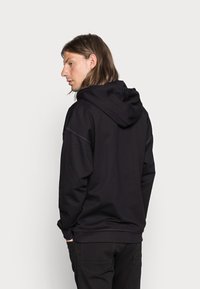 Black hoodie with a smooth texture, featuring a drawstring hood and subtle seams. Worn with black pants, shown from the back.