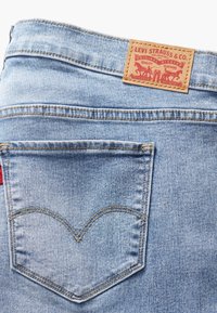 Jean en denim bleu clair présentant une poche arrière avec des coutures orange et un patch en cuir Levi Strauss à la ceinture.