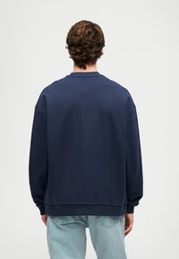 Sudadera azul marino con cuello redondo, corte holgado y puños acanalados, hecha de un tejido suave. Combinada con jeans de color azul claro.