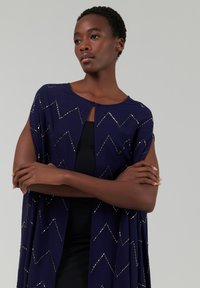 Marineblauer Cardigan mit Zickzack-Silberakzenten. Weicher Stoff, offenes Vorderteil, kurze Ärmel, mit einem subtilen Glanz und lässigem Design.