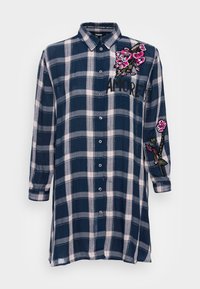 Marinblå och vit rutmönstrad skjorta med långa ärmar, knäppning framtill och broderade blommor. Har en avslappnad passform och rundad nederkant.