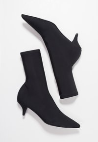 Černé kotníkové boty vyrobené z elastického materiálu s špičatou špičkou a štíhlým podpatkem typu kitten heel; mají bezproblémový design.