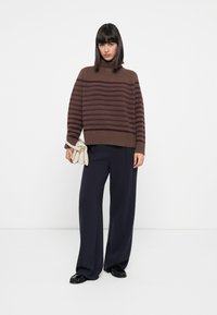 Maglione a collo alto a righe marrone e bordeaux con vestibilità rilassata, abbinato a pantaloni a gamba larga navy e una borsa beige.
