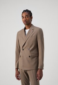 Giacca tailleur beige doppiopetto in tessuto leggero con revers a scollatura, due tasche frontali e bottoni neri. Design slim-fit.