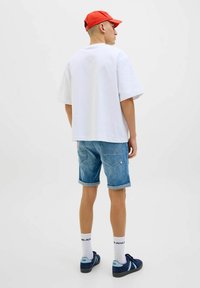 Witte T-shirt met korte mouwen, blauwe denim shorts met opgerolde zomen, marineblauwe sneakers en een rode pet. Eenvoudig ontwerp zonder opvallende patronen of texturen.