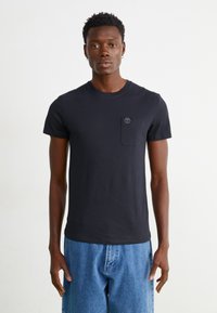 Tricou din bumbac negru cu guler rotund, mâneci scurte și un buzunar pe piept stâng, cu un logo mic. Design simplu, cu o croială ajustată.