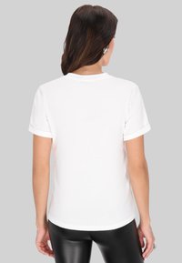 Hvid kortærmet t-shirt med optrukne manchetter, der har en rund halsudskæring og en glat tekstur, båret med sorte tætsiddende bukser.