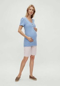 Top texturizado azul claro com mangas curtas e decote em V, apresentando três botões. Combinado com calções rosa claro e sapatos slip-on castanhos.