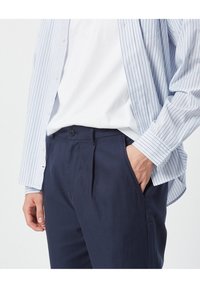 Camicia blu chiaro a righe con bottoni sopra una t-shirt bianca, abbinata a pantaloni classici a pieghe di colore blu navy scuro. Presenta una chiusura con bottoni e tasche.
