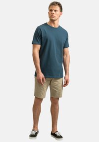 Teal katoenen t-shirt met korte mouwen, ronde halslijn, gecombineerd met beige shorts en zwarte sneakers. De pasvorm is casual en ontspannen.