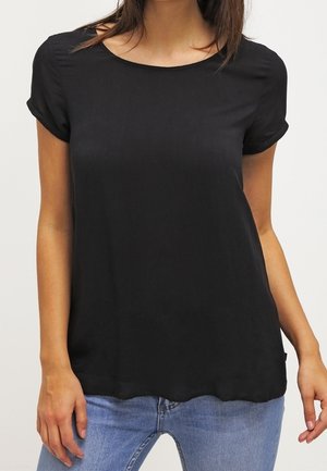 Woman wearing a plain black short-sleeve t-shirt paired with light blue jeans, standing against a plain background.