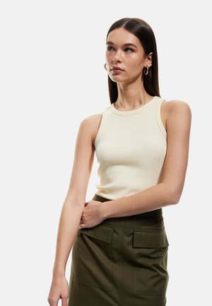 Geribbelde, mouwloze top in roomkleur, met een ronde halslijn. Gecombineerd met een donker olijfgroene rok met twee vo pockets. Glad textuur.