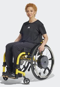 Juodas sportinis marškinėliai su logotipu, juodos kelnės ir juodi batai. Geltonas vežimėlis su sidabrinėmis ratų, juodais priedais ir mažais ratukais.