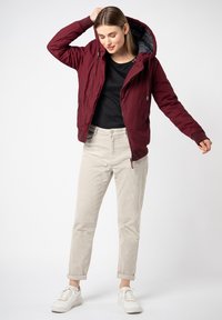 Burgundy zip-up jacket with a hood and gray lining, paired with beige corduroy pants and white sneakers. The jacket features side pockets.