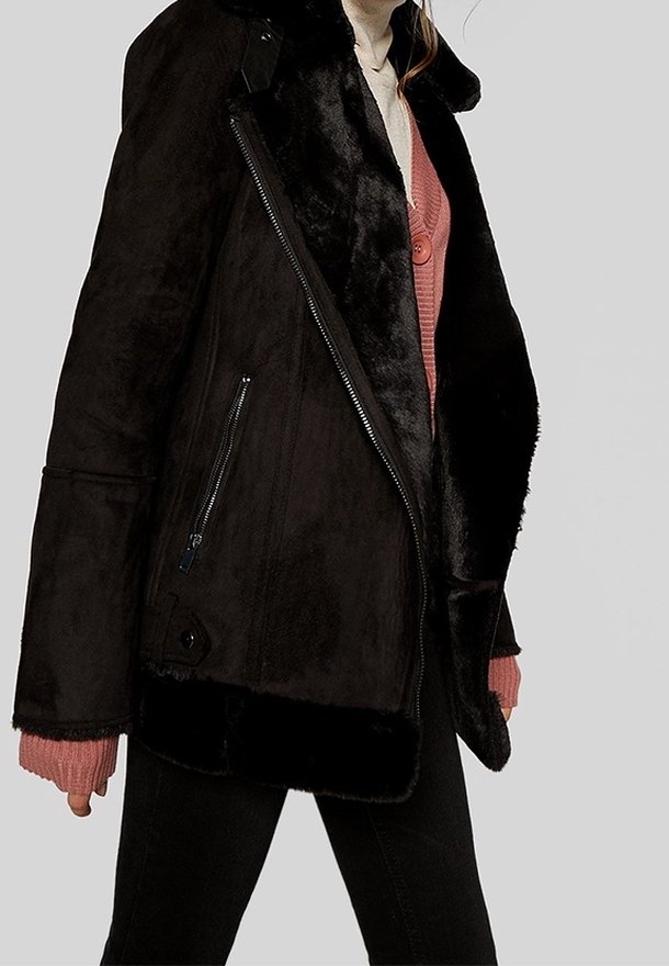 Chaqueta de pelaje sintético negro con un bolsillo lateral con cremallera, cuello ancho y textura suave, con mangas de gran tamaño y forro acolchado.