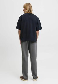 Czarna, oversize t-shirt z krótkim rękawem, połączona z szarymi dresami. Materiał wydaje się miękki, z luźnym krojem i minimalistycznym detalem na plecach.