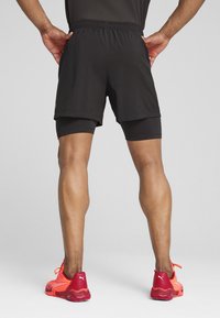 Schwarze Sportshorts mit einem elastischen Bund, die über eng anliegenden schwarzen Shorts getragen werden, kombiniert mit leuchtend roten Sportschuhen.