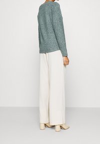 Pitkähihaista, teal-väristä neulepaitaa, jolla on tekstuuripinta, on yhdistetty leveälahkeisiin, kermaisiin housuihin ja korkokenkiin, jotka ovat vaaleanbeigejä.