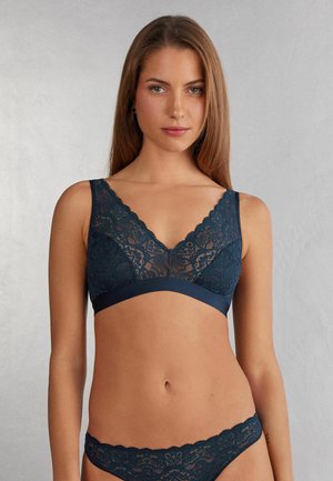 Marineblauwe kant bralette met gegolfde randen en een V-halsontwerp, met daaronder een contrasterende gladde band en bijpassende kanten slip.