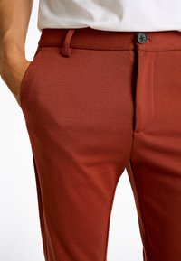 Rostfärgade skräddarsydda byxor av texturerat tyg, med rak passform, sidofickor och knappstängning.