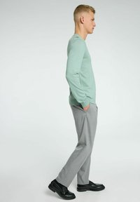 Chemise à manches longues vert clair associée à un pantalon gris et des chaussures noires. La chemise a un design simple et une texture douce.