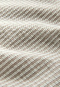 Gros plan sur un tissu texturé beige et blanc avec des rayures verticales nervurées alternées et des rainures.