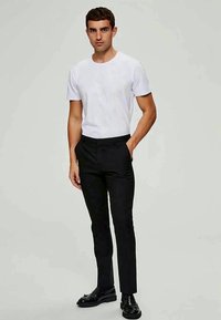 Camiseta branca de gola redonda combinada com calças pretas de corte slim. Os sapatos são de couro preto, adicionando um contraste elegante ao conjunto. Design simples no geral.