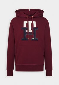 Sweat à capuche bordeaux avec poche avant et grands lettrages "TH" blancs et bleu marine ainsi que logo sur la poitrine.