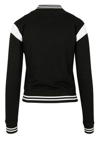 Zwarte varsityjack met witte mouwstrepen, geribbelde manchetten en kraag. Gemaakt van zacht materiaal, met een getailleerde pasvorm en een cropped lengte.