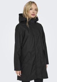 Svart vanntett jakke med hette, trykknapp-lukking, sidelommer og rett snitt. Glatt tekstur, minimalistisk design, urban stil.