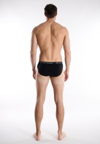 Black briefs with an elastic waistband featuring "TOM TAILOR" logo. Smooth material, fitted design, and minimal rear coverage.