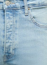 Lichtblauwe denim jeans in close-up die de voorzak, riemlus, stikseldetails en een metalen knoop met gegraveerde tekst toont.