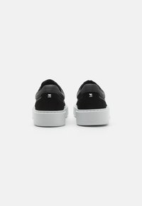 Sorte semskede plattformsneakers med hvite gummisåler, med minimalistisk design og sølvfargede nagler på hælen.