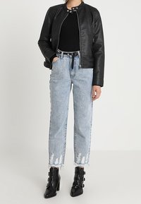 Femme portant une veste en cuir noir, un haut noir, un jean déchiré bleu clair avec des ourlets effilochés, et des bottines à sangle à boucle noires.