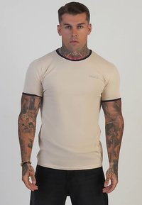 Beige figursydd t-shirt med korta ärmar och marinblå ribbad krage. Har en diskret logga på bröstet och texturerade tygdetaljer.