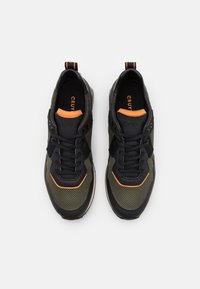 Baskets de sport noires et vert olive avec des panneaux en mesh, des accents texturés, des détails orange et des lacets noirs, avec une languette au talon.